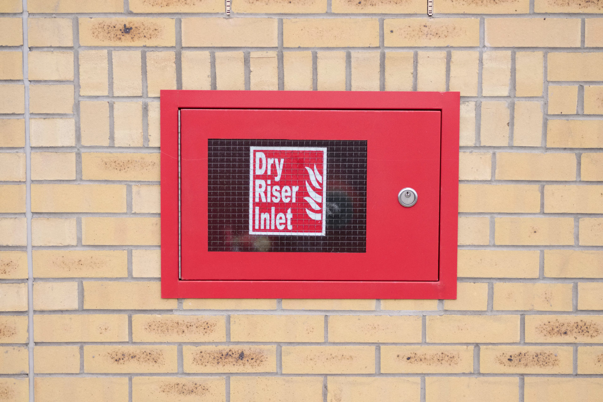 Dry riser inlet box red on brick wall for emergency fire services water connection for hose brigade engine at shopping mall retail park