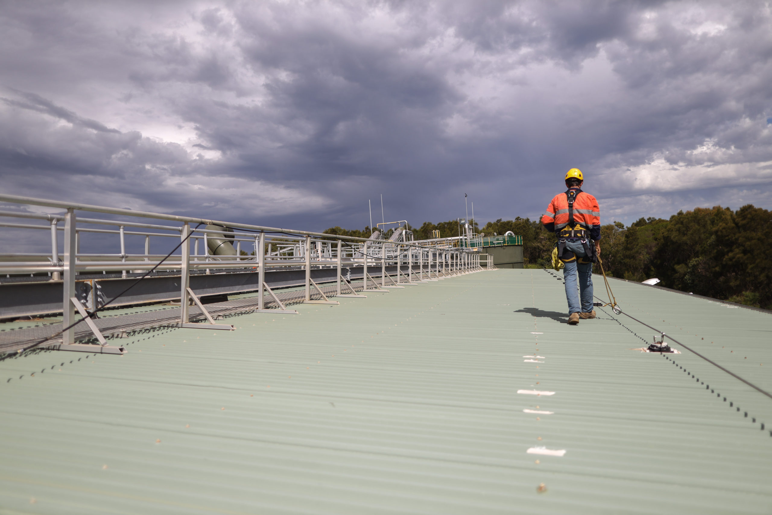 Construction safety inspector wearing fall safety harness walking on the roof by clipping safety rope on fall arrest, fall restraint   horizontal safety line while inspecting fixed roof anchor points